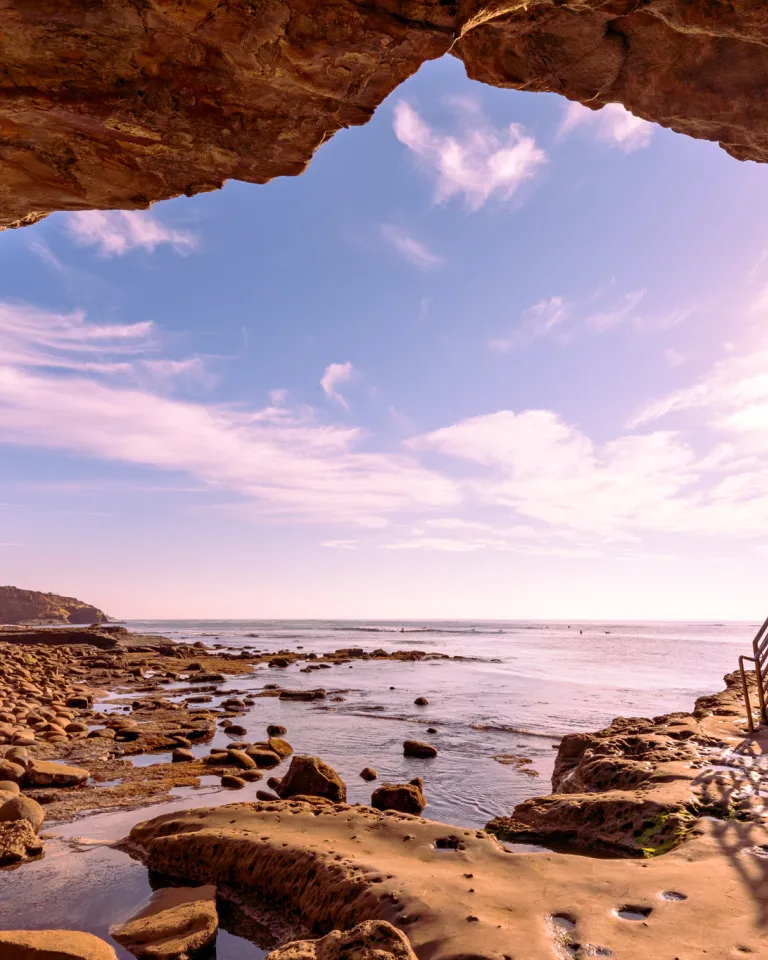 View from inside a rocky seaside cave in Point Loma looking out to the ocean, with a staircase on the right and sunlight streaming through the entrance.