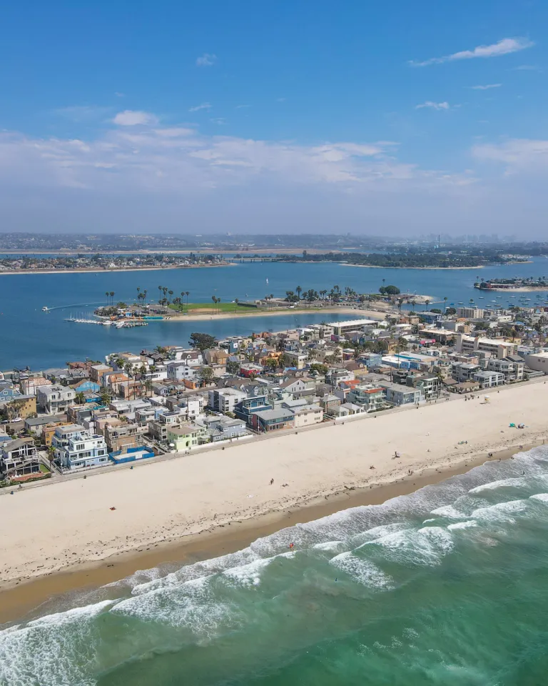 Aerial of Mission Beach boardwalk and waterfront houses and vacation rentals with Mission Bay in the background